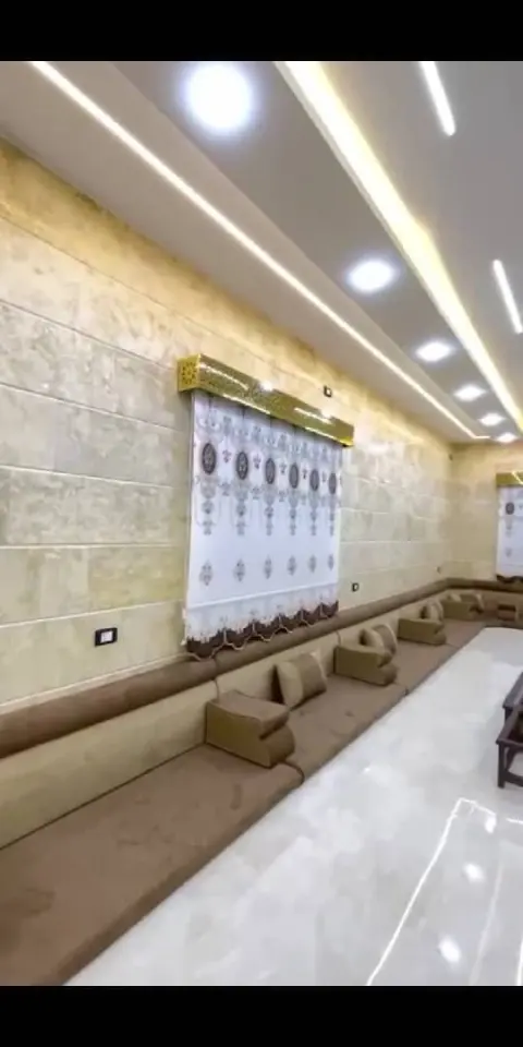 مجلس عربي أرضي بلون بني على طول القاعة مع ستارة رومانية مطرزة وكرنيش ذهبي