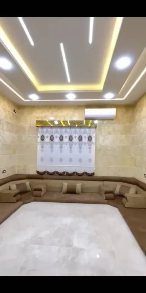 قاعة مجلس عربي بجلسات بنية وسجادة بيضاء وإضاءة سقف مخفية