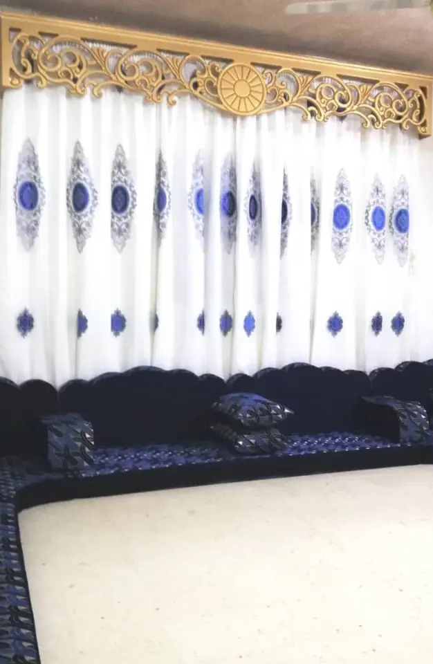 ستارة تول بيضاء مطرزة بميداليات زرقاء تحت كرنيش ذهبي محفور فوق مجلس كحلي