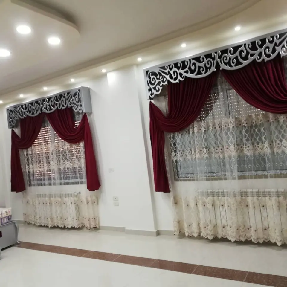 ستائر مخمل خمري منسدلة تحت كرنيش فضي محفور مع تول مطرز على نافذتين